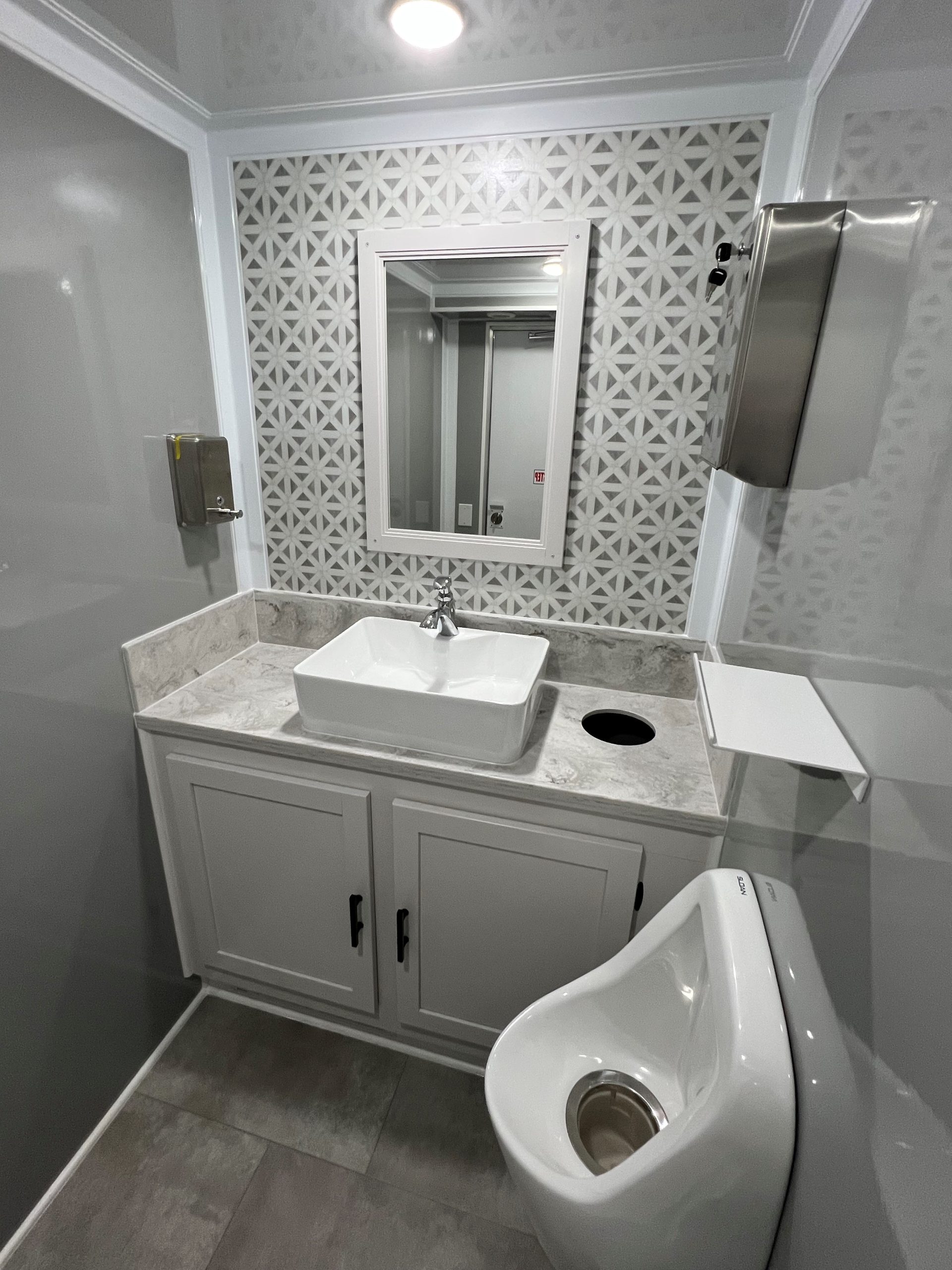 Vanity with vessel sink, tile backsplash and urinal inside an NRT restroom trailer